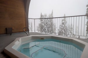Un jacuzzi en un balcón con vista a árboles cubiertos de nieve.
