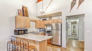 A modern kitchen with wooden cabinets, a stainless steel refrigerator, and a bar area with stools. - Chateau on the Ridge by Okanagan Premier (Beaverdell)