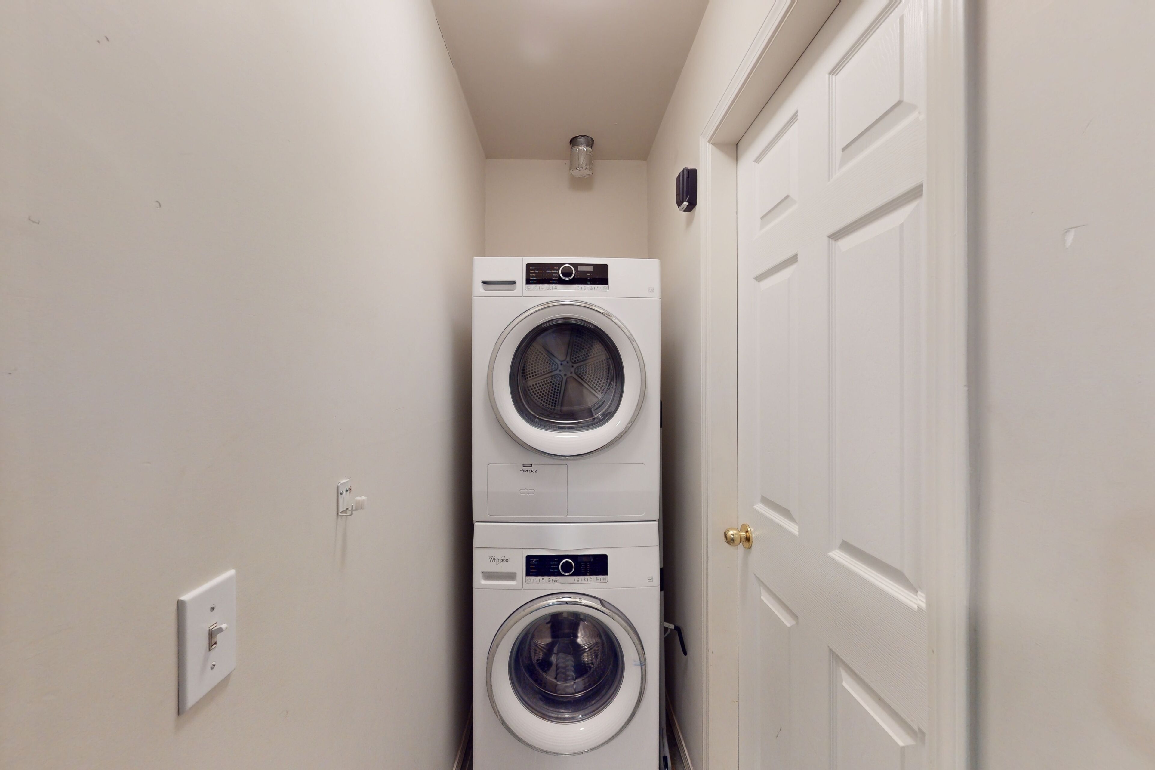 A laundry room with two stacked washing machines and a door.