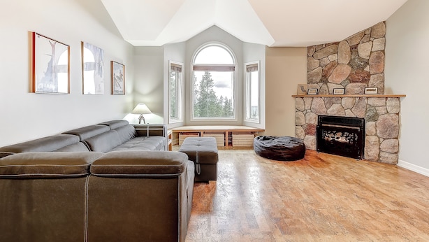 A modern living room with a stone fireplace, a sectional sofa, and a bench by the window. - Chateau on the Ridge by Okanagan Premier (Beaverdell)