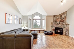 Un salon moderne avec une cheminée en pierre, un canapé d’angle et un banc placé près de la fenêtre.