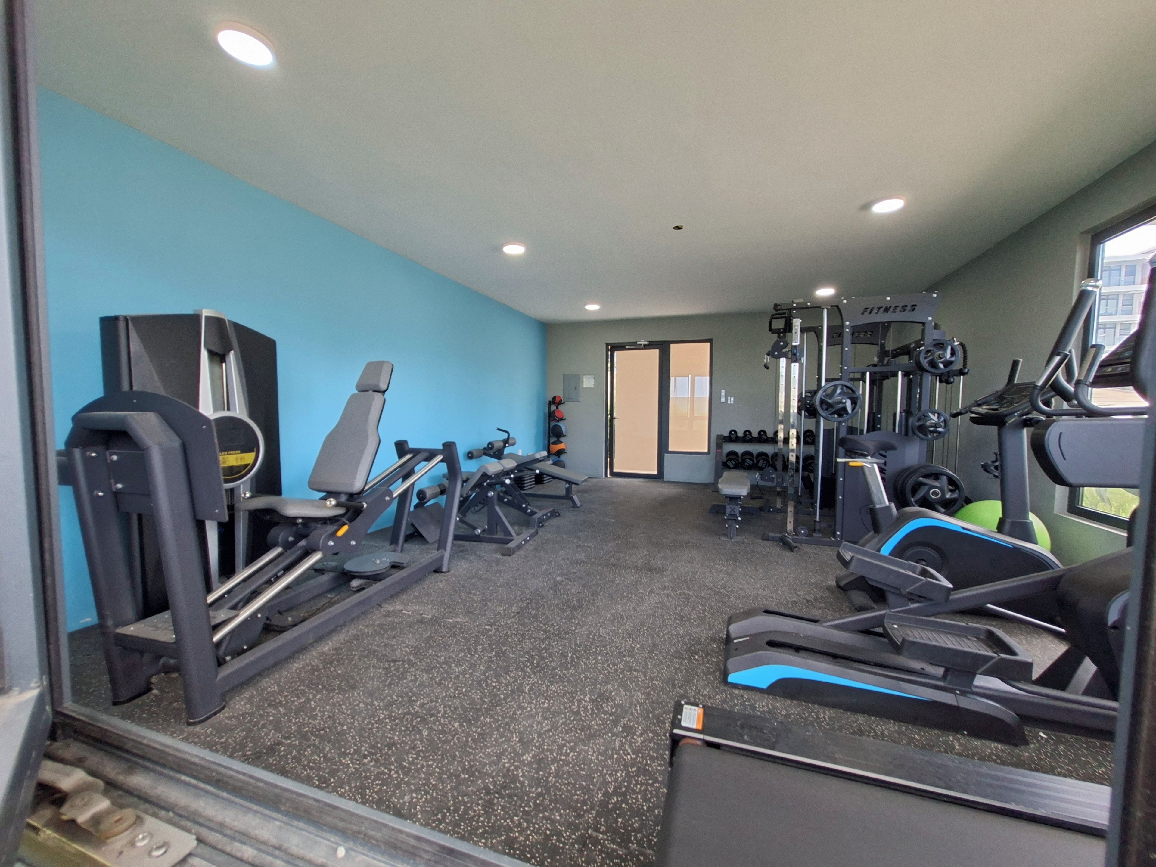 A gym with various exercise equipment, including treadmills and weight machines, against a blue wall.