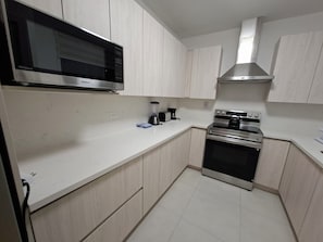 Eine Küche mit hellem Holzkorpus, einer Edelstahl-Mikrowelle, einer Kaffeemaschine und einem Backofen.