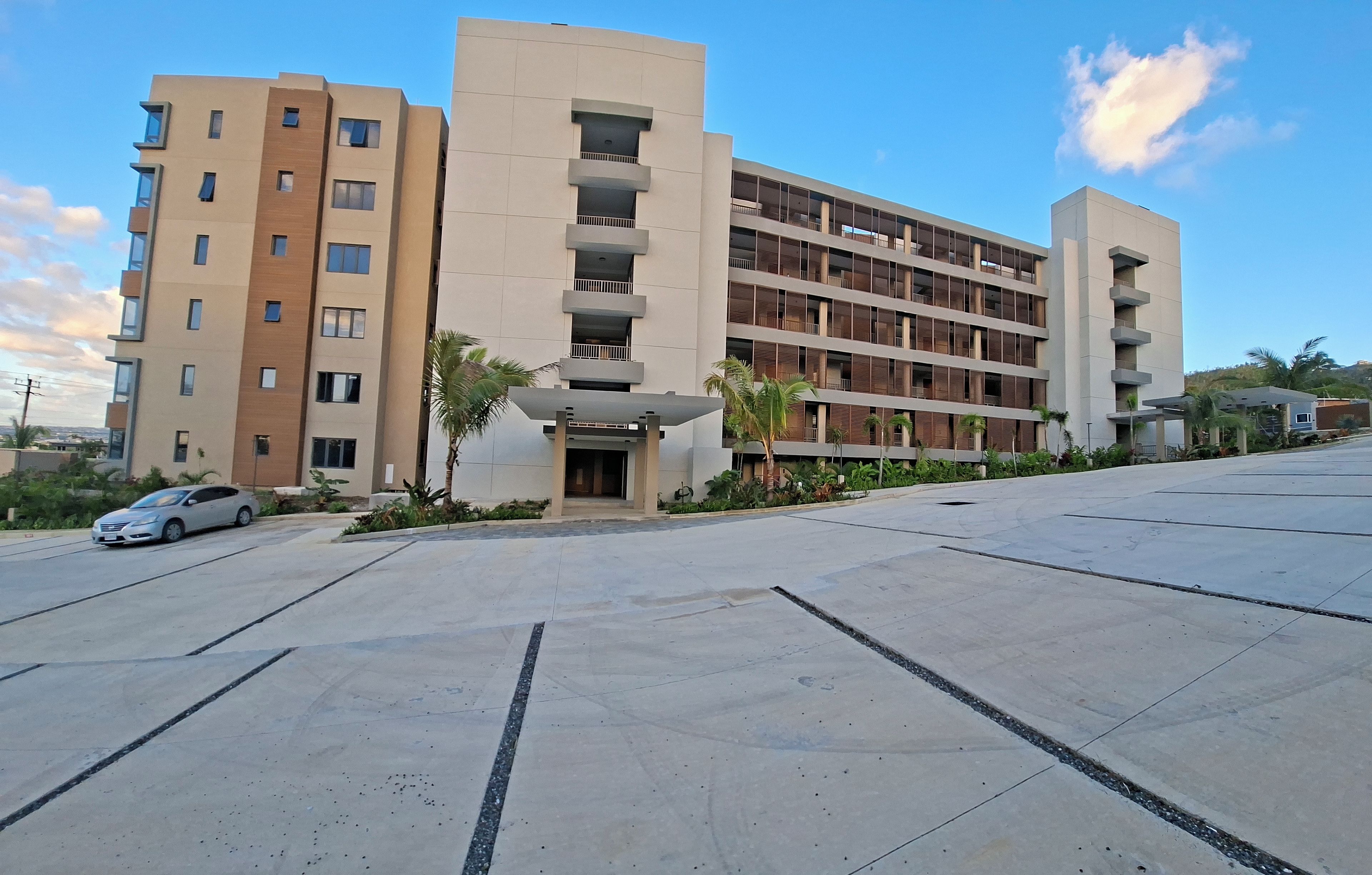 A multi-story hotel with a central entrance, a parking lot, and a clear sky.