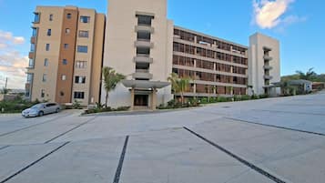 A multi-story hotel with a central entrance, a parking lot, and a clear sky.