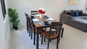 Ein Essbereich mit einem Holztisch, schwarzen Stühlen und einer Blumenvase. Ein graues Sofa und ein Gemälde sind an der Wand zu sehen.