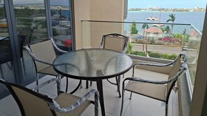 Ein Balkon mit Glastisch und Stühlen, der auf ein Gewässer und eine ferne Stadtansicht blickt.