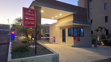 A hotel entrance with a welcome sign, directional arrows, and a security stop sign.