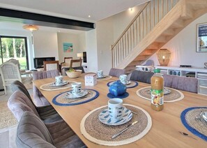 Uma sala de jantar com uma mesa de madeira posta para refeição, cercada por sofás e cadeiras.