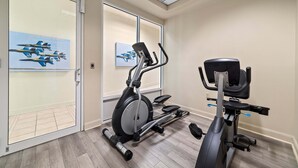 Ett gym med träningsutrustning, en vägg med speglar och en dörr med en utrymningsskylt.