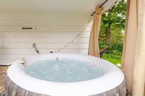 Un jacuzzi en un espacio exterior cubierto con vistas a un jardín, toma de corriente e iluminación con guirnaldas.