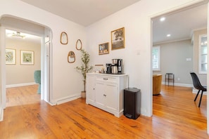Una habitación amplia con pisos de madera, un armario blanco, una cafetera y cuadros en la pared.