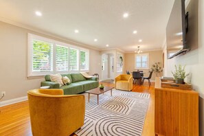 Un amplio salón con un sofá verde, un sillón amarillo y una mesa de comedor con sillas.