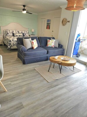 Ein Wohnzimmer mit einer Couch, einem runden Couchtisch und einem Bett mit gemusterten Bettbezügen.