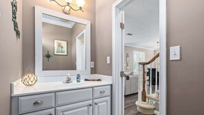 A bathroom with a large mirror, a sink, and a vanity with drawers. - Blue Heron on May Vacation Rental (St. Augustine)