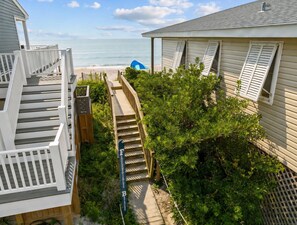 Une propriété située en bord de mer, avec un escalier menant à la plage, une tente bleue et un panneau indiquant « Plage des contes de fées ».