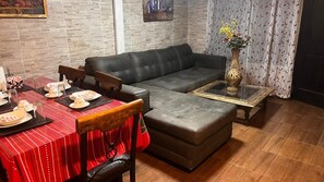 Un salon comprenant un canapé, un pouf, une table à manger avec des chaises et un vase posé sur une table basse.