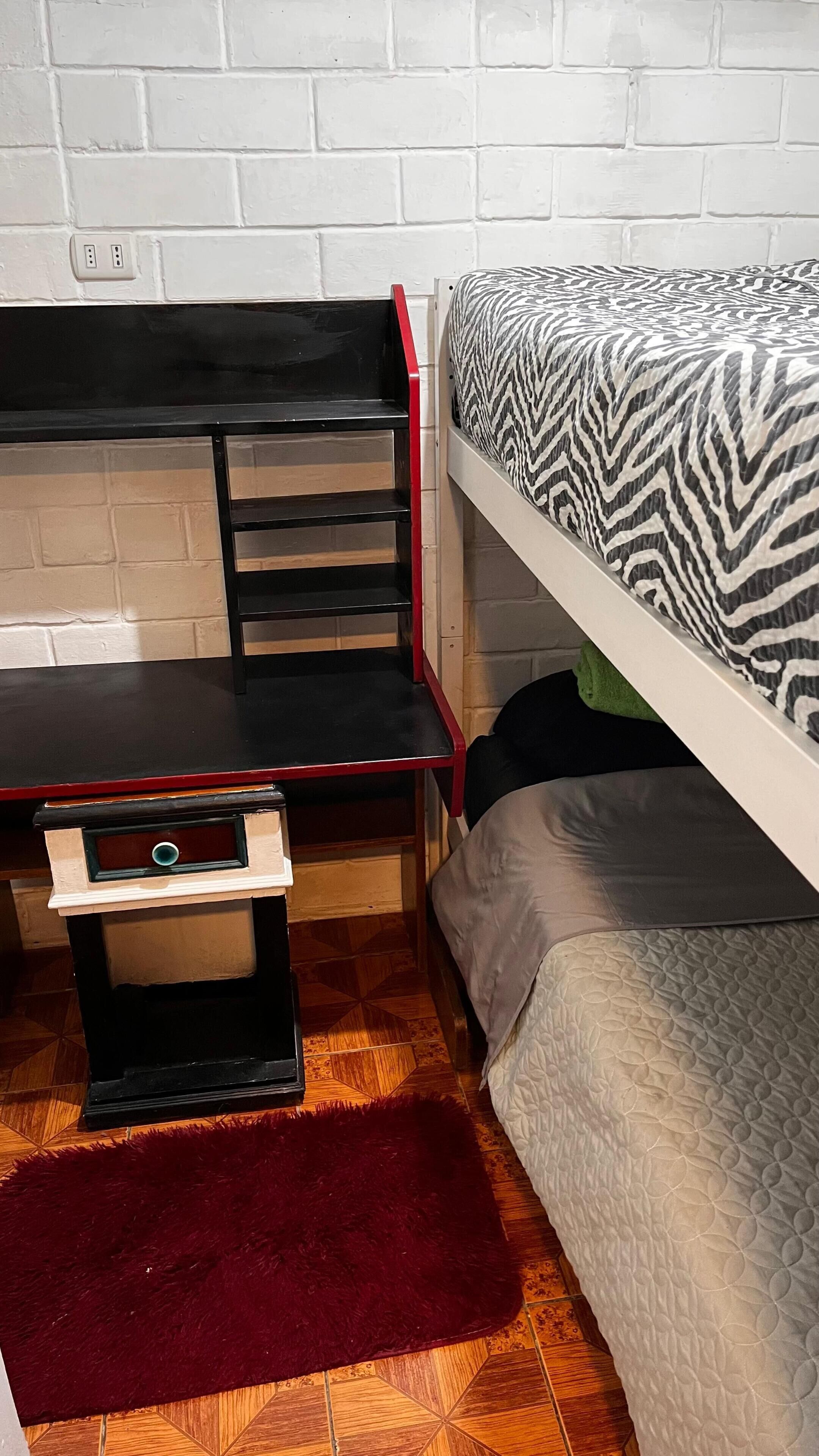 A room with a bunk bed, a desk with a chair, and a red rug on the floor.