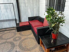 Un coin salon avec des coussins rouges, une plante en pot et un sol carrelé.