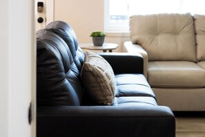Ein modernes Wohnzimmer mit einem dunkelbraunen Ledersofa, einem beigefarbenen Sofa und einem kleinen runden Tisch mit einer Pflanze.
