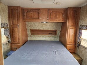 Ein kompaktes Wohnmobil-Interieur mit einem Bett, Holzschränken und einer eingebauten Ablage.