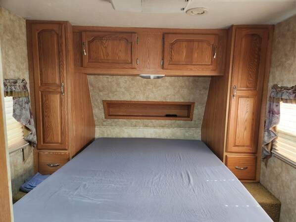 Een ruimtelijk RV-interieur met een bed, houten kastjes en een ingebouwd schap.