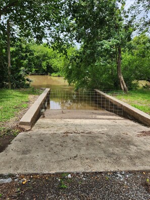 Eine Betonbrücke über ruhigem Gewässer, umgeben von üppiger Vegetation und Bäumen.