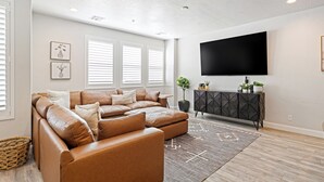 Ein Wohnzimmer mit einem Ecksofa, einem Flachbildfernseher und einem dekorativen Schrank.