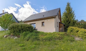 Ein einstöckiges Haus mit geneigtem Dach, umgeben von üppigem Grün und blauem Himmel.