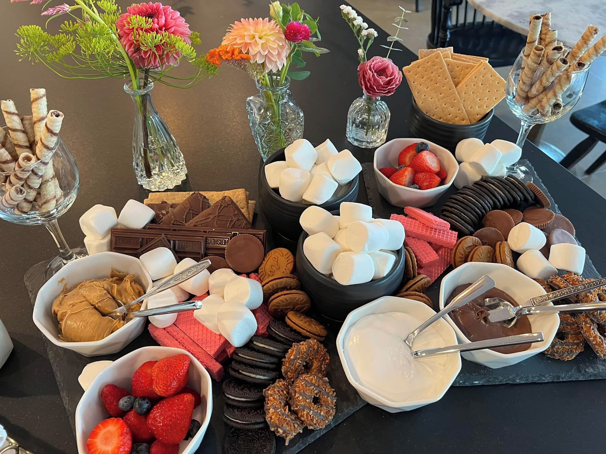 A table with various food items including marshmallows, chocolate, cookies, and fruits.