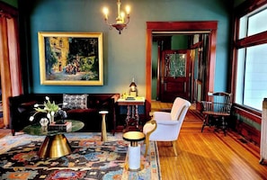 A room with a large painting, a chandelier, a sofa, a chair, a table, and a patterned rug.
