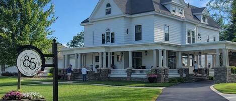 A large, two-story white building with a porch, stone steps, and a sign indicating it is a boutique hotel.