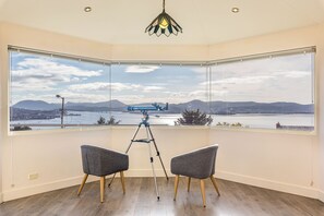 A room with a large window, two chairs, a tripod, and a hanging light fixture. - A Spacious Hillside Retreat with Panoramic Views (Sandy Bay)