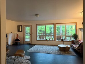 Ein geräumiges Wohnzimmer mit großem Fenster, einem runden Couchtisch, einer Couch und einem Sessel.