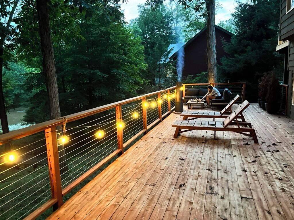 A wooden deck with a railing, benches, and a person cooking on a grill.