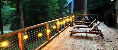 A wooden deck with a railing, benches, and a person cooking on a grill.