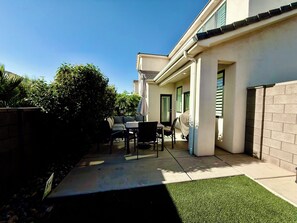 Un patio con tavolo e sedie, un barbecue coperto e un piccolo giardino.