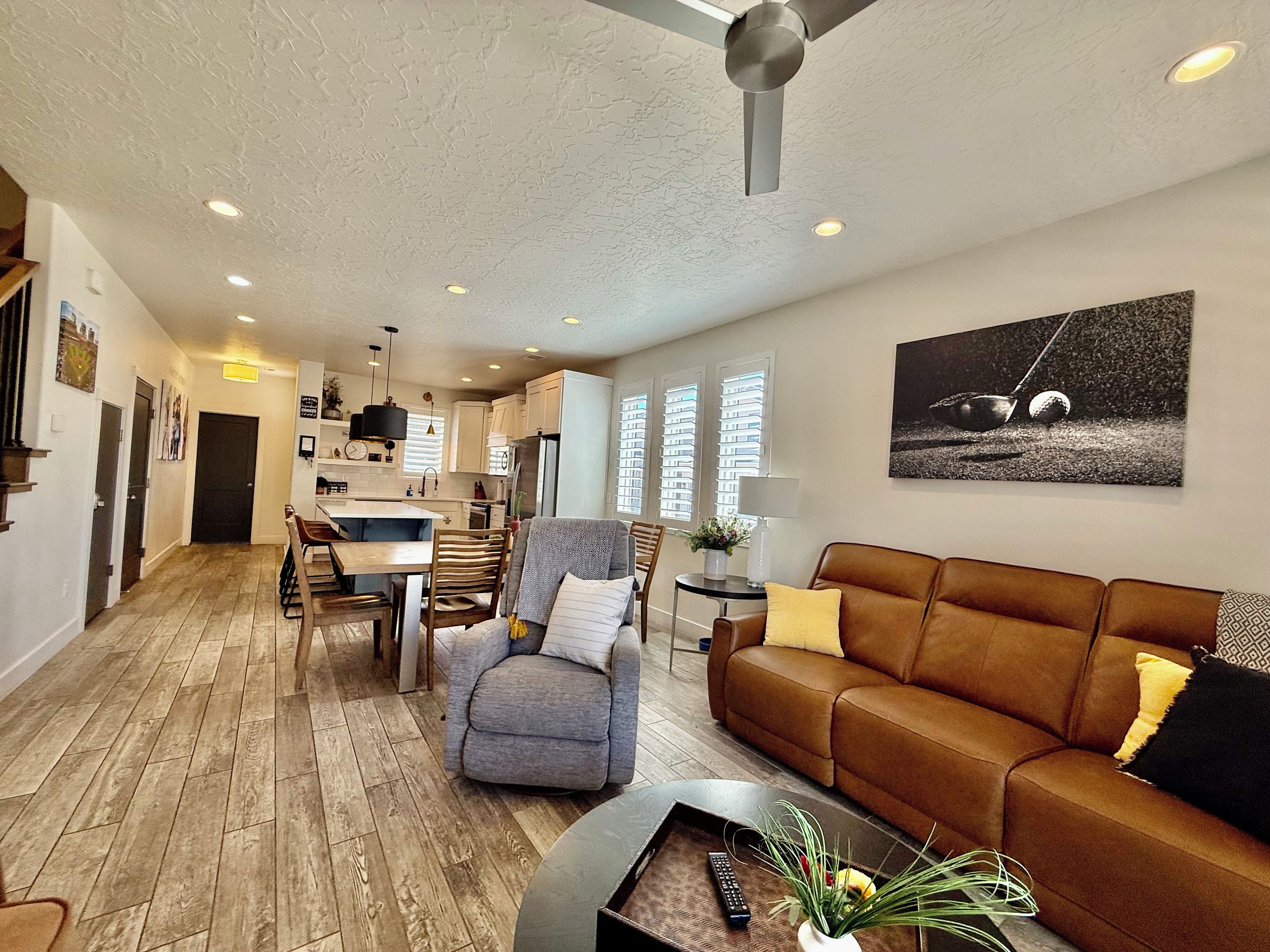 A modern living room with a brown leather sofa, a grey armchair, and a dining area with wooden flooring.