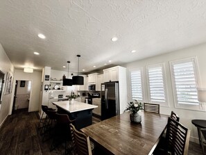 Une cuisine moderne avec des meubles blancs, un îlot central et un coin repas doté de chaises en bois.