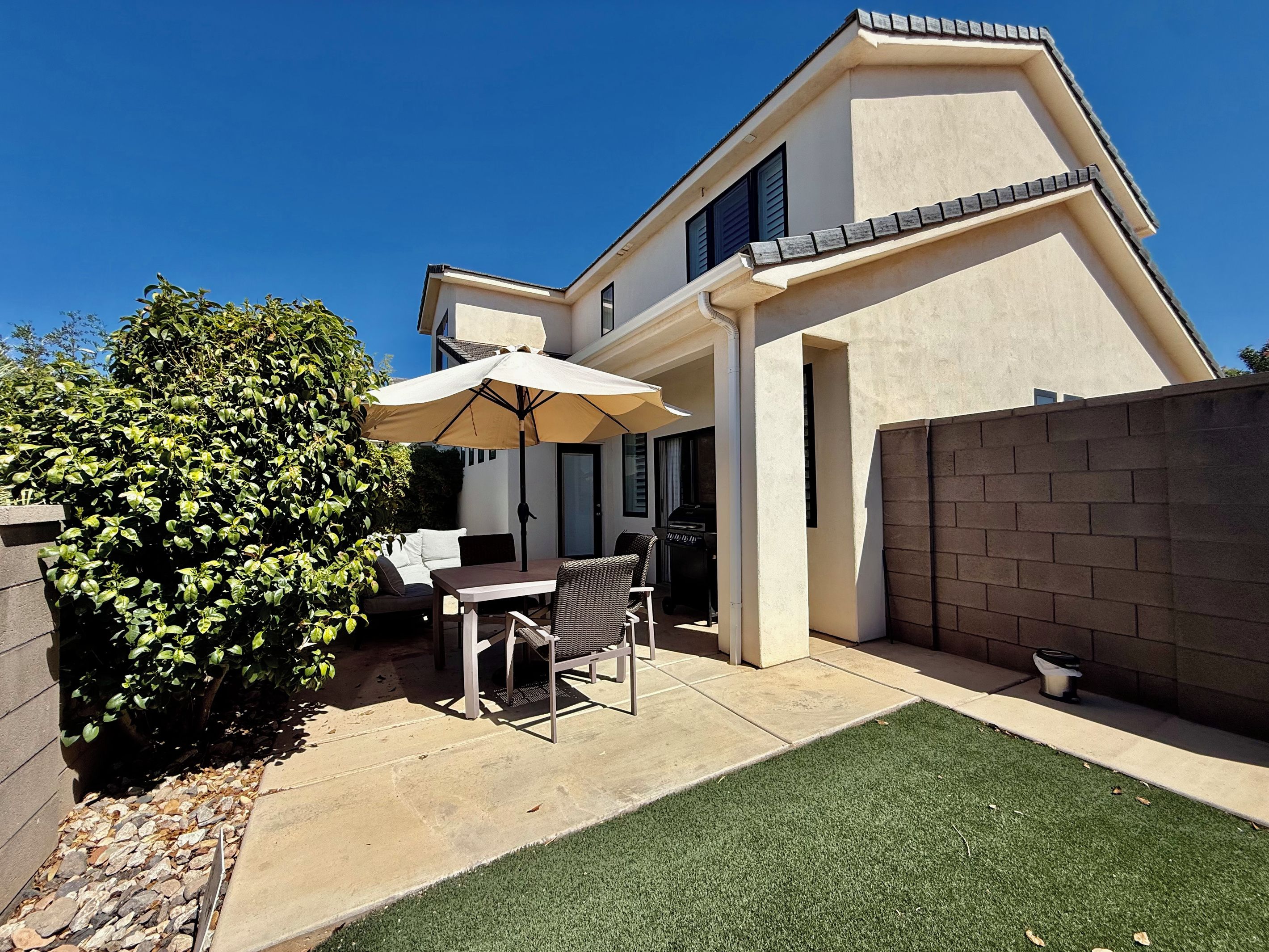 A residential property with a patio area featuring a table and chairs, a barbecue grill, and a well-maintained lawn.