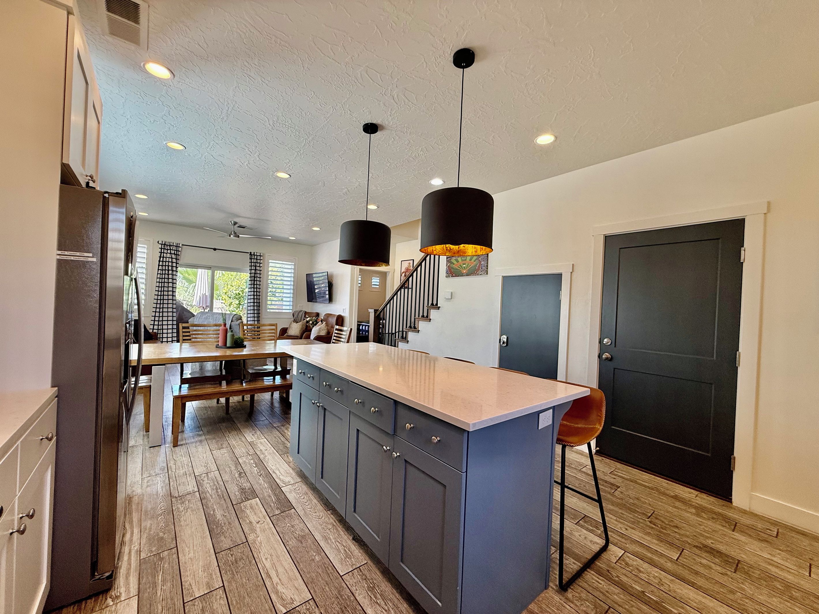 A modern kitchen with a central island, wooden flooring, and pendant lighting.