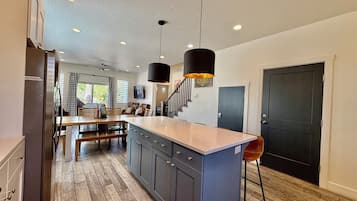 A modern kitchen with a central island, wooden flooring, and pendant lighting.