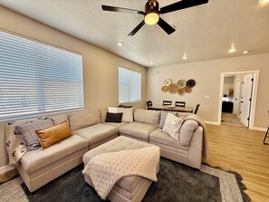 Uma sala de estar com sofá seccional, ventilador de teto e espaço de jantar com mesa e cadeiras.