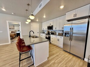 A modern kitchen with a central island, stainless steel appliances, and white cabinetry. - Desert Base Camp | Lazy River + Hot Tub (Hurricane)