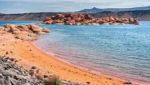 A beach with clear water, a rocky outcrop, and distant mountains.