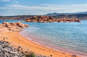 A beach with clear water, a rocky outcrop, and distant mountains. - Desert Base Camp | Lazy River + Hot Tub (Hurricane)