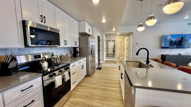 Una cocina moderna con electrodomésticos de acero inoxidable, armarios blancos y piso de madera.