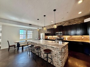 Una cocina con una isla grande, armarios oscuros e iluminación colgante.