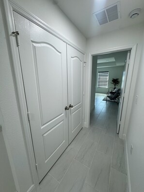 Ein Flur mit weißen Türen, einem Deckenventil und Blick in einen Raum mit Sessel und Pflanze.