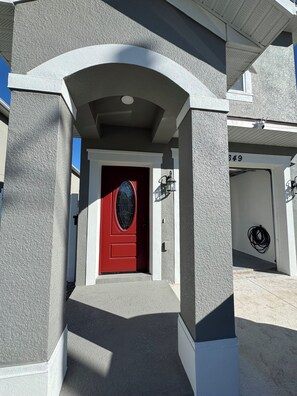 Ein Gebäudeeingang mit roter Tür, Fenster mit weißem Rahmen und einer Garagenummer 649.